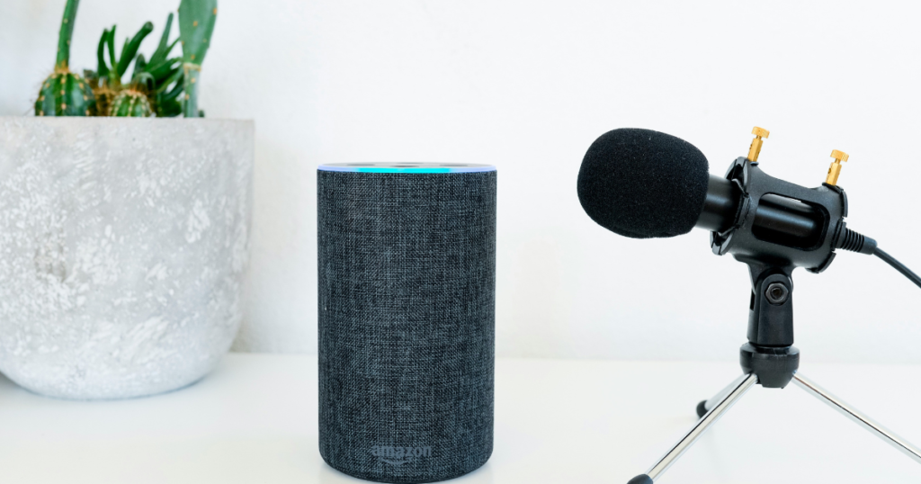 A sleek Amazon Echo smart speaker and a professional studio microphone on a white desk, illustrating the voice-command technology