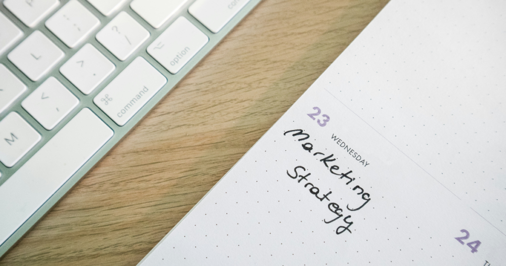 A handwritten marketing strategy on a dotted notebook page, positioned next to a keyboard, symbolizing the transition from traditional planning to AI-powered digital marketing workflows.